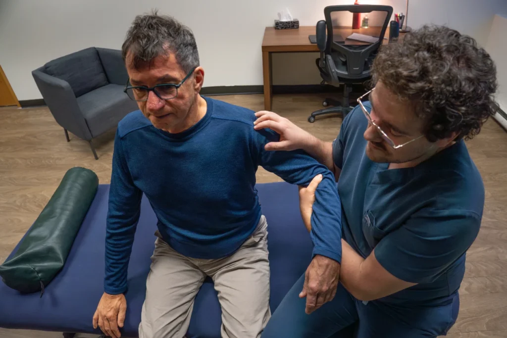 Praticien en ostéopathie accompagnant les mouvements du bras d’un patient en position assise