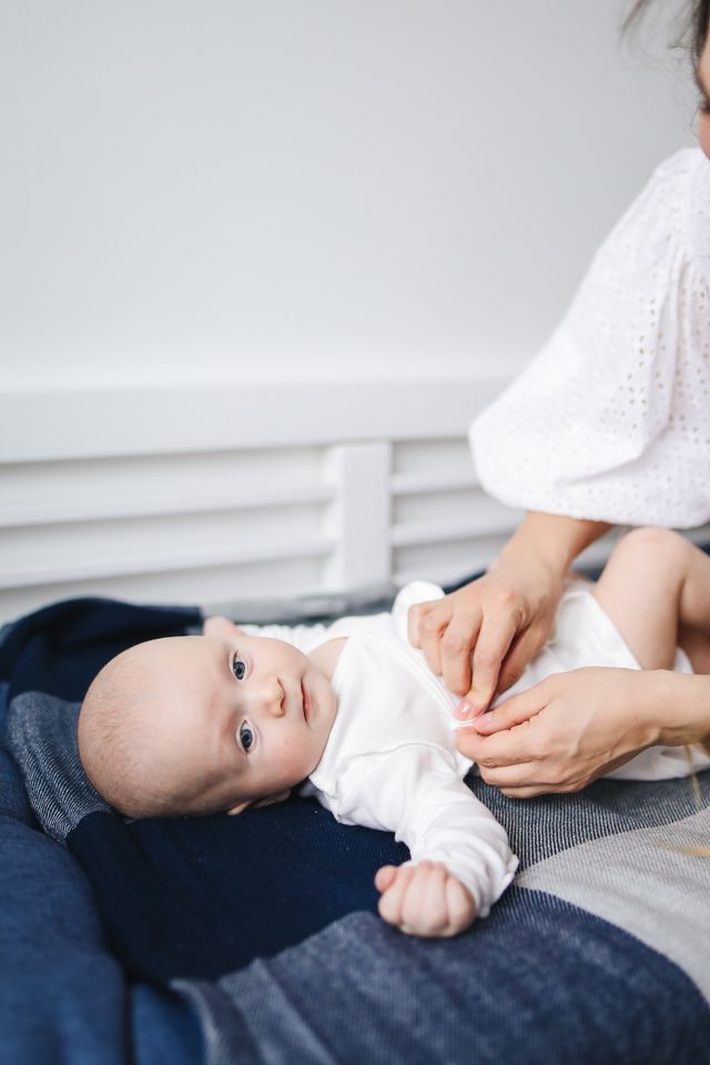 Un parent habille son bébé allongé sur une couverture.